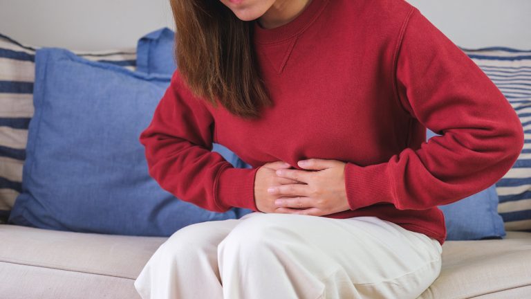 Woman experiencing abdominal pain while sitting on a couch