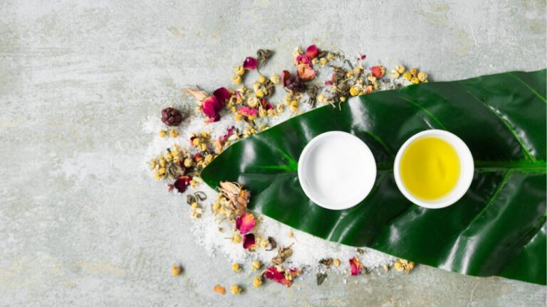 Herbal oil and cream with dried flowers on a green leaf.