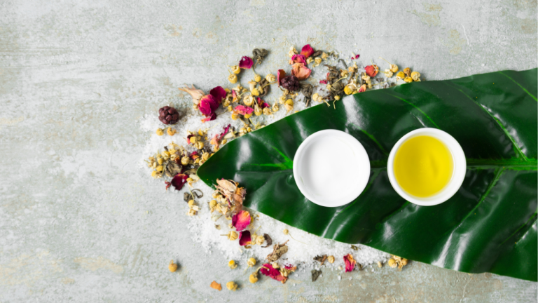 Herbal oil and cream with dried flowers on a green leaf.