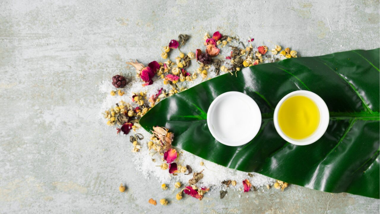 Herbal oil and cream with dried flowers on a green leaf.