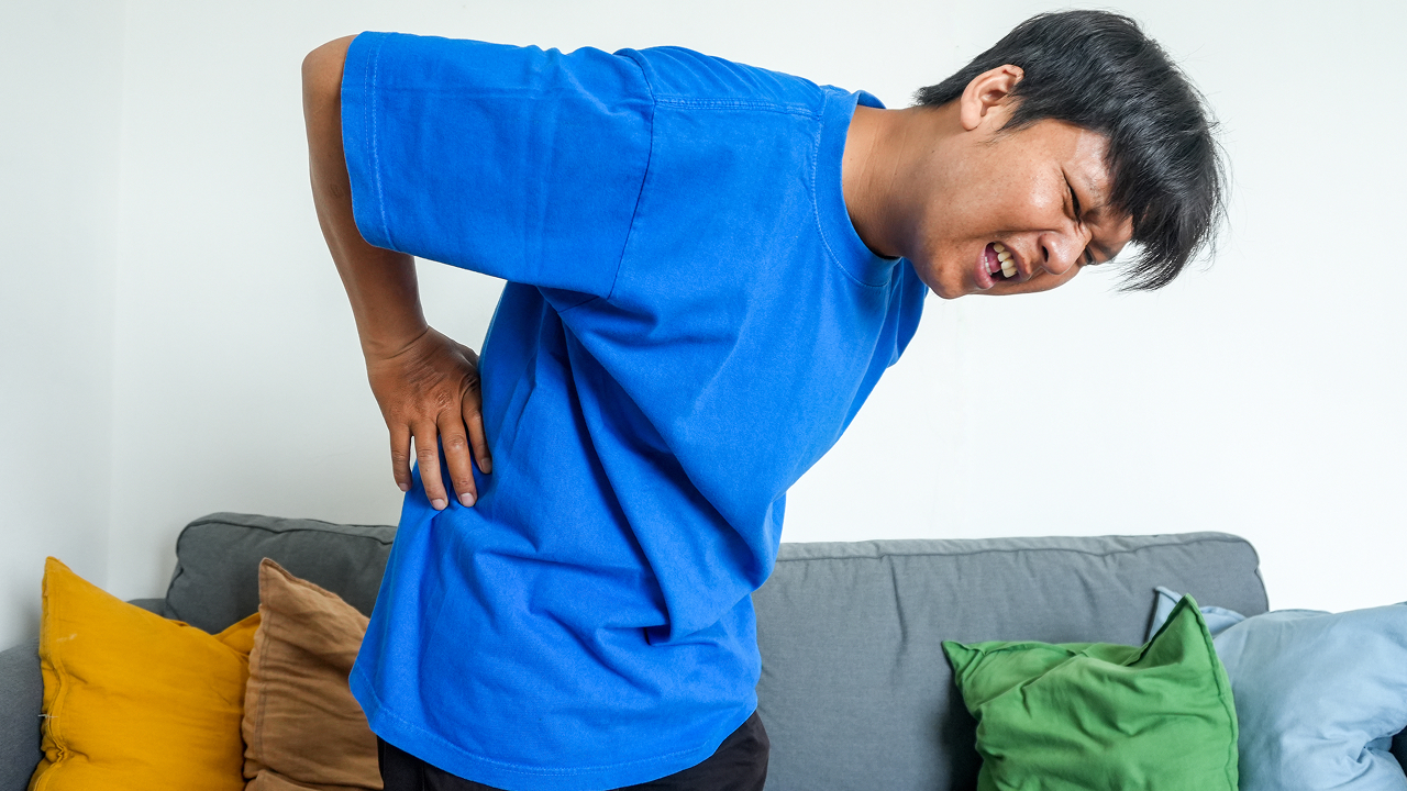 Man experiencing lower back pain while sitting on a bed.